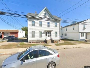 Pawcatuck apartment for rent - A silver car is parked in front of a white house with a porch.