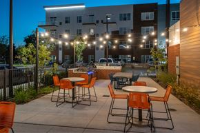 Hampton apartment for rent - A patio with orange chairs and tables is set up in front of a building.