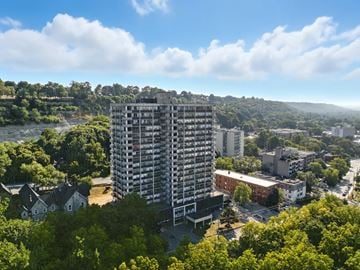 Hamilton apartment for rent - A tall building stands in the middle of a town with a river and trees in the background.