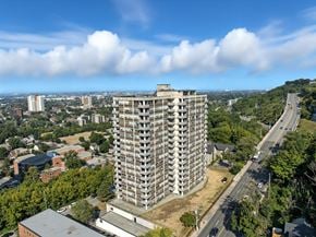 Hamilton apartment for rent - A tall building with many windows is surrounded by trees and other buildings.