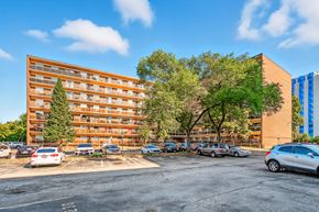 Burlington apartment for rent - A parking lot with cars and a multi-story building with trees in front.