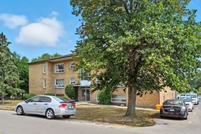 Oakville apartment for rent - A silver car is parked on the side of the road in front of a tree and a building.
