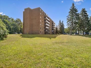 Barrie apartment for rent - A tall brown building with a grassy field in front of it.