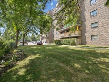 Orillia apartment for rent - A tree-lined pathway leads to a building with balconies.