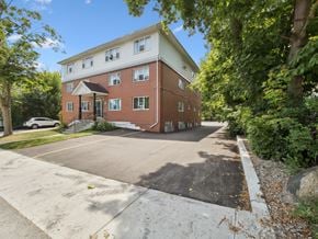 Orillia apartment for rent - A red brick building with a white trim and a parking lot in front.