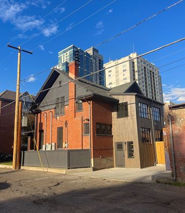 Denver apartment for rent - A red brick building with a black roof and a grey fence in front of it.