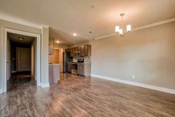A large empty room with wooden floors and a kitchen area in the background.