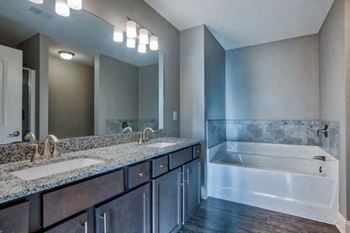 A bathroom with a large mirror, two sinks, and a bathtub.