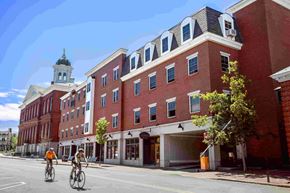 Exeter apartment for rent - Two people riding bicycles on a street in front of a red brick building.