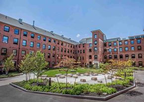 Biddeford apartment for rent - A courtyard with a garden in front of a red brick building.
