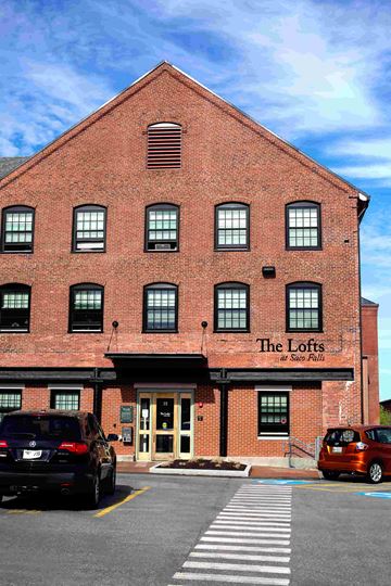 Biddeford apartment for rent - The Lofts at Stone Pits is a red brick building with a parking lot in front.