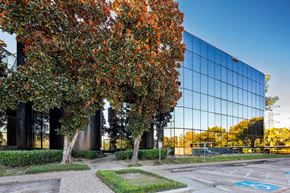 Houston apartment for rent - A modern building with a glass facade is surrounded by trees with orange leaves.