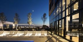Montréal apartment for rent - A modern building with a pool and lounge chairs in front.