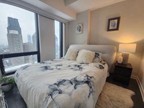 Montréal apartment for rent - A bedroom with a large bed and a city view through the window.