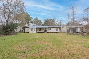 Lafayette house for rent - A house with a white exterior and a brown roof is surrounded by a grassy yard.