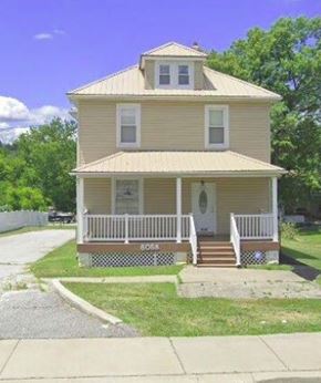 Baltimore apartment for rent - A yellow house with a porch and a sign that says "BOOK".