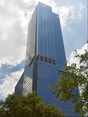 New York apartment for rent - A tall skyscraper with a glass facade stands under a partly cloudy sky.