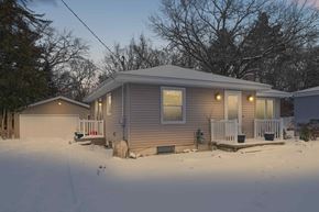 Grand Rapids house for rent - A house with a grey siding and a white porch is surrounded by snow.