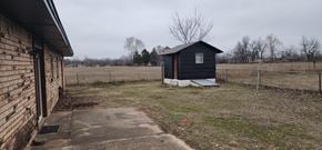 Harrah house for rent - A small black shed sits in a grassy field.