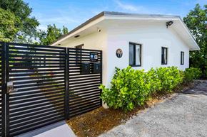 Miami triplex for rent - A white house with a black gate and a small garden in front.