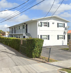 Miami apartment for rent - A white two-story house with a black fence and hedges on the side.