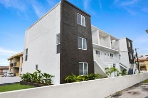 Miami apartment for rent - A modern two-story building with a white and grey exterior and a landscaped front yard.