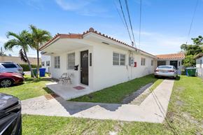 Miami triplex for rent - A white house with a red tile roof and a small front yard.
