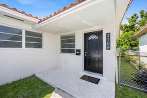 Miami triplex for rent - A white house with a black door and a mailbox on the wall.