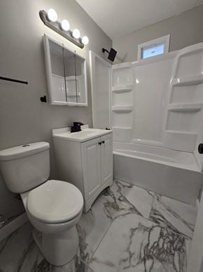 Gary house for rent - A white toilet sits next to a white sink in a marble bathroom.