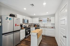 Von Ormy house for rent - A kitchen with white cabinets and a wooden island.