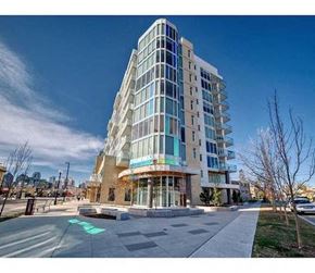 Calgary apartment for rent - A modern multi-story building with a glass facade and a green arrow painted on the sidewalk in front of it.