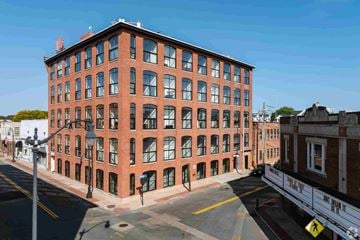 Attleboro apartment for rent - A red brick building with many windows is on a street corner.
