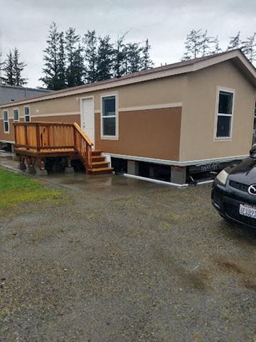 Crescent City apartment for rent - A beige mobile home with a wooden deck and a car parked in front.