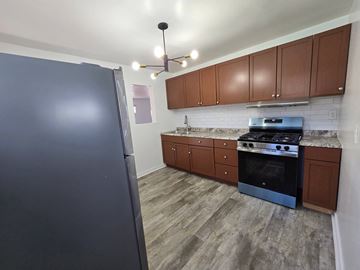 Gary house for rent - A kitchen with a black fridge, wooden cabinets, and a black stove top oven.
