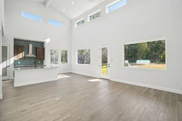 Horseshoe Bay house for rent - A spacious room with wooden floors and white walls, featuring a kitchen area with a stove and a countertop, as well as several windows and pictures on the walls.