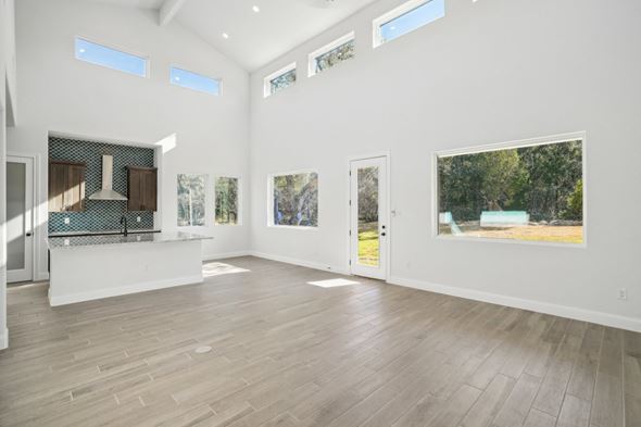 Horseshoe Bay house for rent - A spacious room with wooden floors and white walls, featuring a kitchen area with a stove and a countertop, as well as several windows and pictures on the walls.