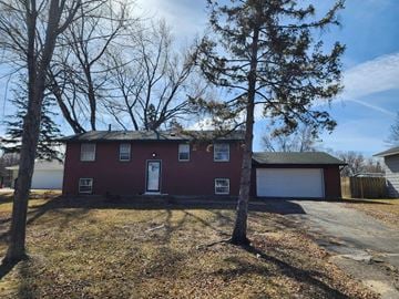 Coon Rapids house for rent - A red house with a white door and windows is surrounded by trees.