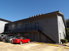 Dallas apartment for rent - A red car is parked in a parking lot in front of a building.