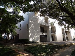 Dallas apartment for rent - A white building with balconies is surrounded by trees.