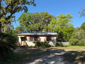 Palatka house for rent - A small house with a red door and windows is surrounded by trees and vegetation.