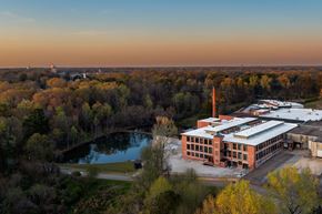 Monroe apartment for rent - A large building with a long white chimney is surrounded by trees and a body of water.