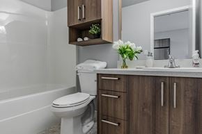 Saskatoon apartment for rent - A white toilet sits in a bathroom with wooden cabinets and a white tub.