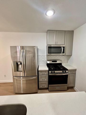 Houston apartment for rent - A kitchen with a stainless steel refrigerator, microwave, oven, and a white counter.