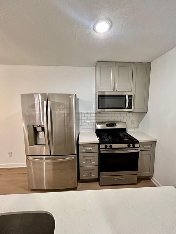 Houston apartment for rent - A kitchen with a stainless steel refrigerator, microwave, oven, and a white counter.