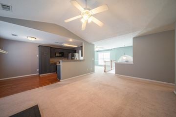 Phenix City house for rent - A spacious living room with a ceiling fan and a kitchen area in the background.