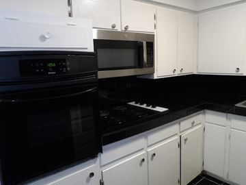 Dallas apartment for rent - A black stove top oven sits next to a black microwave in a kitchen with white cabinets.