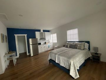 Lakeland apartment for rent - A bedroom with a bed, nightstand, and a kitchen area in the background.