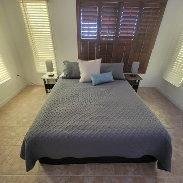 Lakeland apartment for rent - A bed with a grey comforter and two pillows sits in a room with wooden shutters on the window.