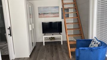 Lakeland apartment for rent - A blue chair sits in front of a television in a room with a painting on the wall and a wooden ladder.
