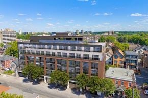 Ottawa apartment for rent - A modern multi-story building with a flat roof is surrounded by other buildings and trees.